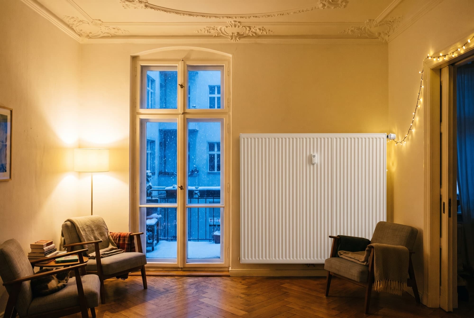 Heizkörper unter einem hohen Altbaufenster in Berlin, Stuckdecke und Fischgrätparkett, Winterabend